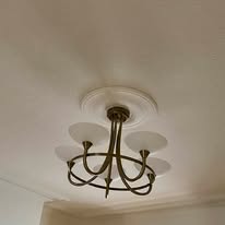 A brass chandelier with five upward-facing frosted glass shades beautifully complements a ceiling adorned with a decorative medallion, expertly installed by an electrician for optimal elegance and functionality.